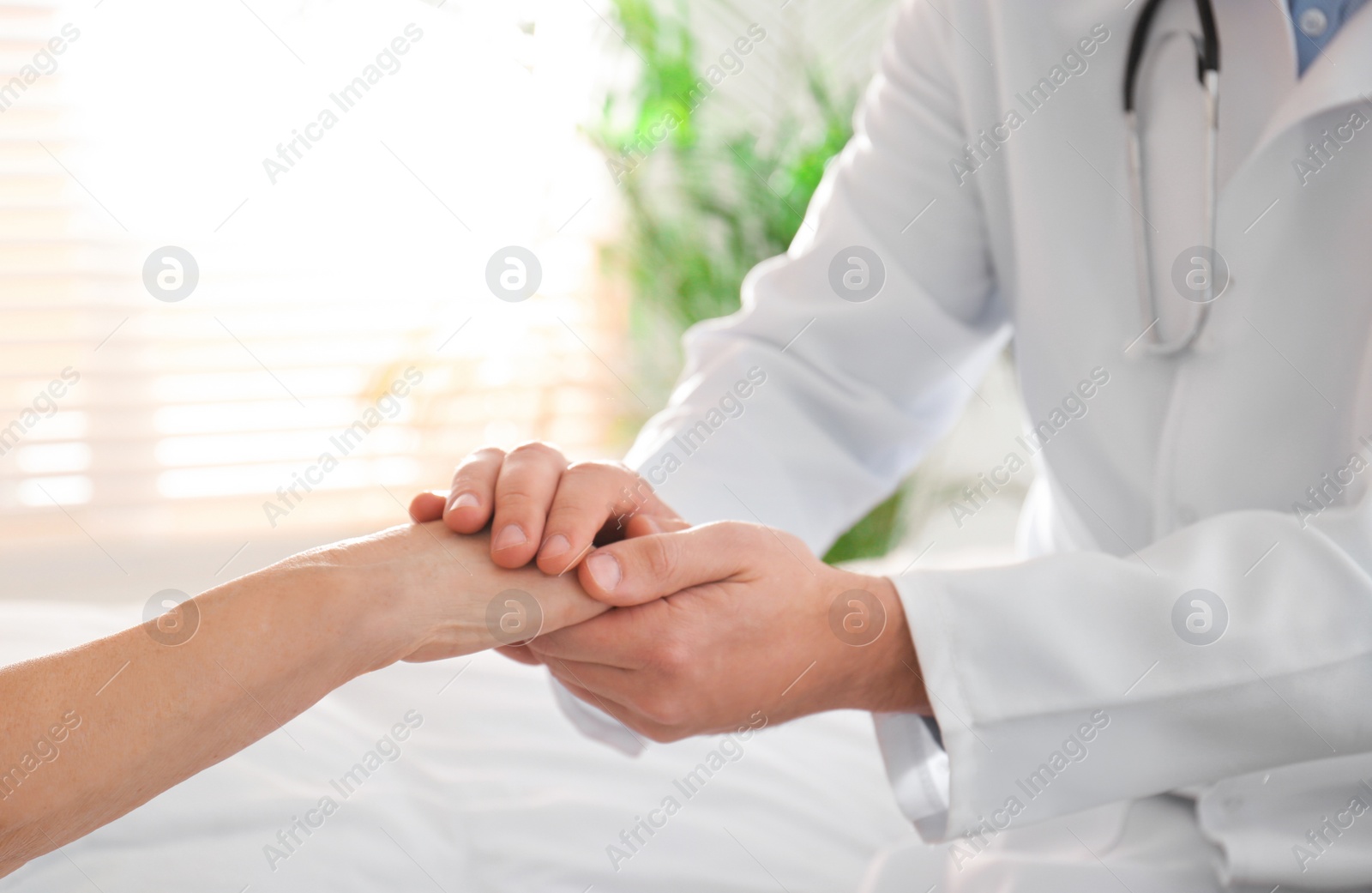 Photo of Doctor and senior patient holding hands in hospital, closeup