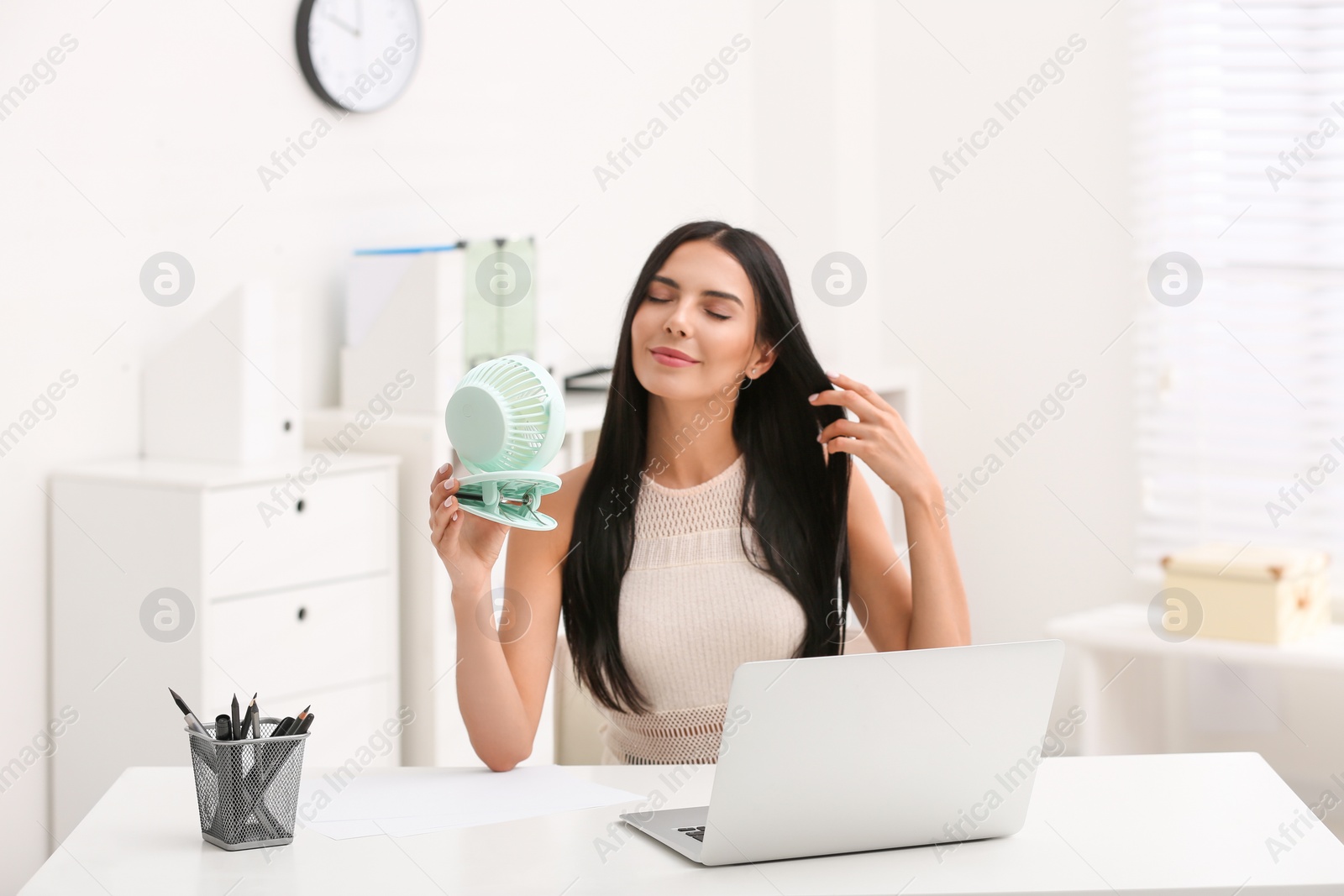 Photo of Young woman enjoying air flow from fan at workplace