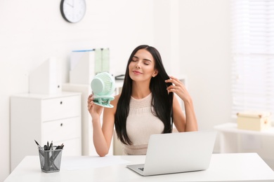 Young woman enjoying air flow from fan at workplace