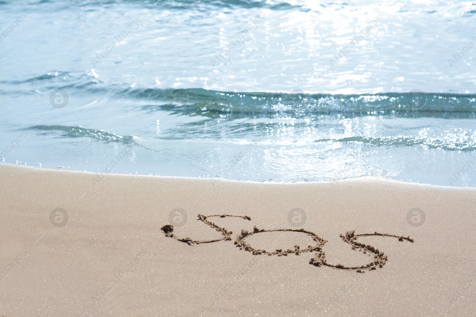 Photo of Message SOS drawn on sandy beach near sea