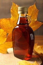 Photo of Bottle of tasty maple syrup and dry leaves on wooden table