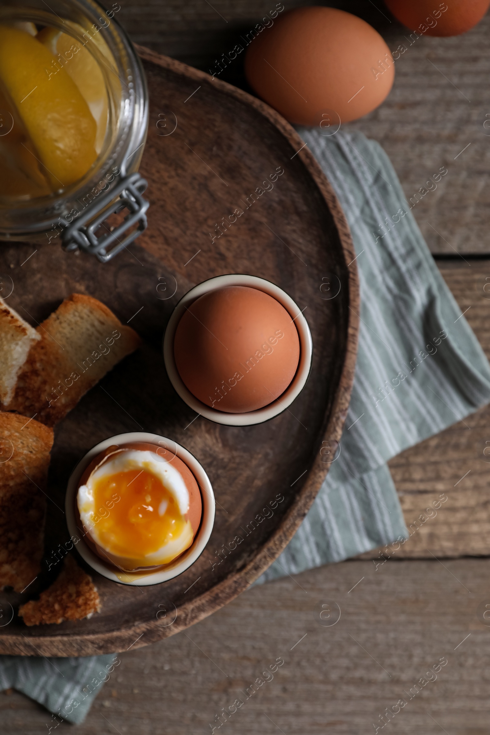 Photo of Tasty boiled eggs in cups on wooden table, flat lay