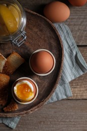 Tasty boiled eggs in cups on wooden table, flat lay