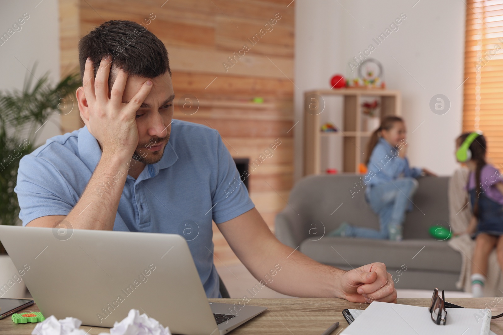 Photo of Children disturbing stressed man in living room. Working from home during quarantine