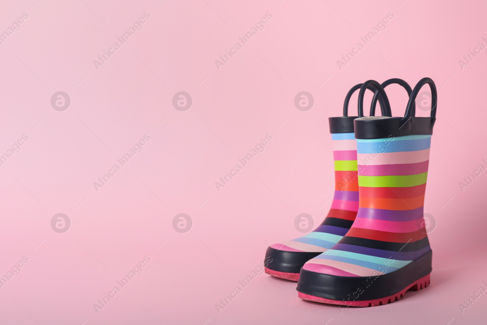 Photo of Pair of rainbow rubber boots on pink background. Space for text