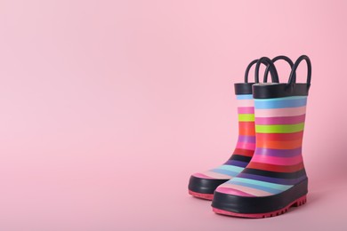 Photo of Pair of rainbow rubber boots on pink background. Space for text