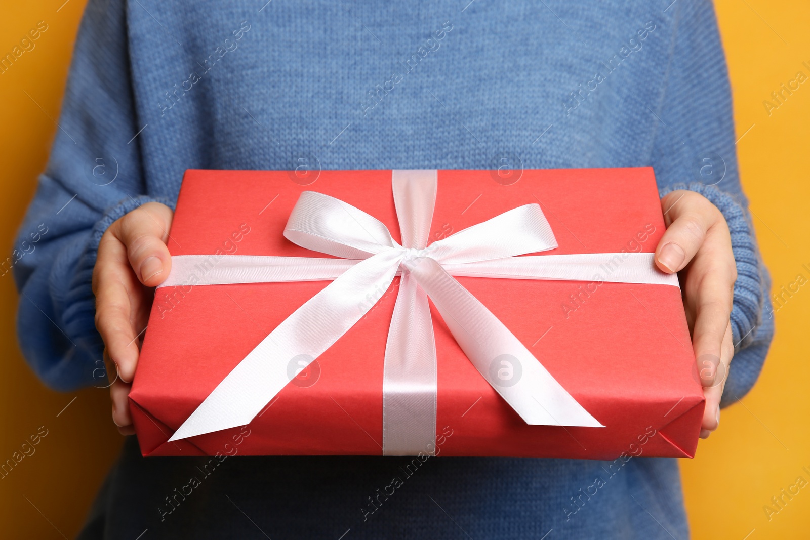 Photo of Woman holding Christmas gift box on yellow background, closeup