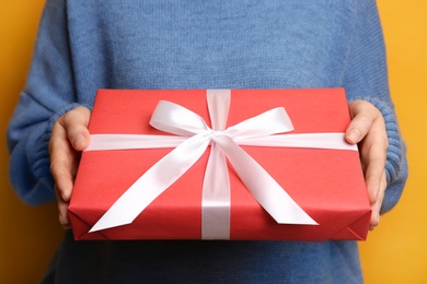 Woman holding Christmas gift box on yellow background, closeup