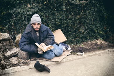 Poor homeless man with book on street in city