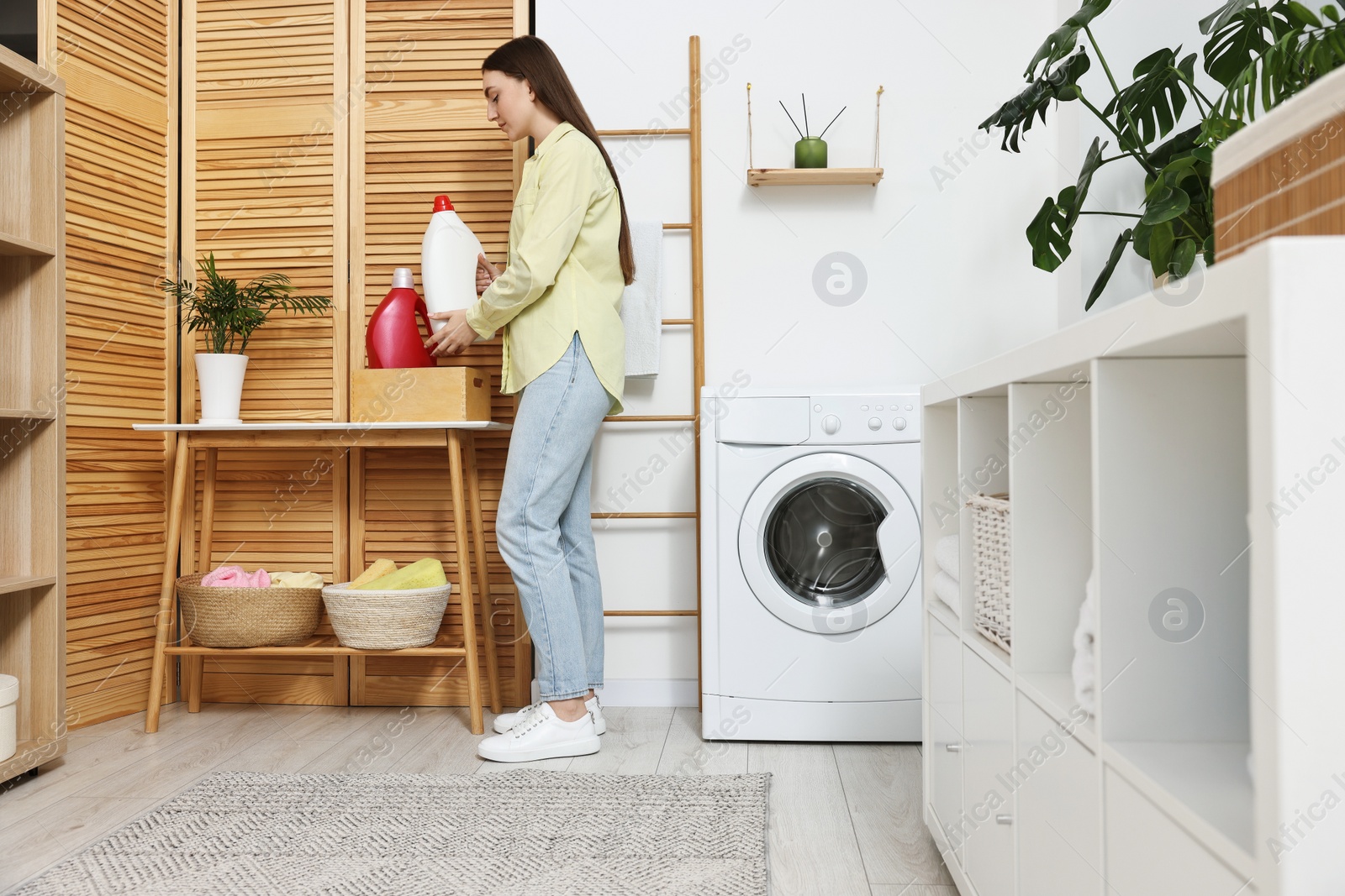 Photo of Beautiful young woman with detergent in laundry room