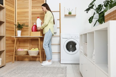 Beautiful young woman with detergent in laundry room