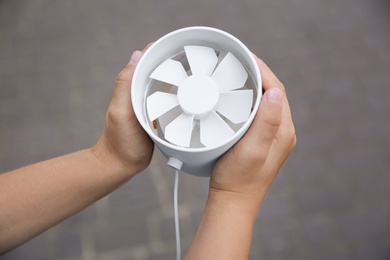 Photo of Little child with portable fan outdoors, closeup. Summer heat