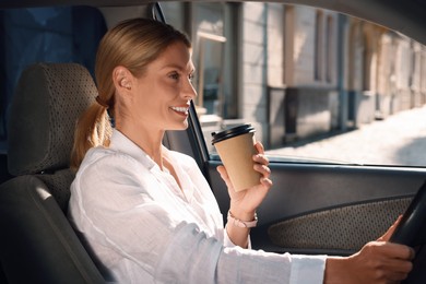 Photo of Coffee to go. Happy woman with paper cup of drink driving her car