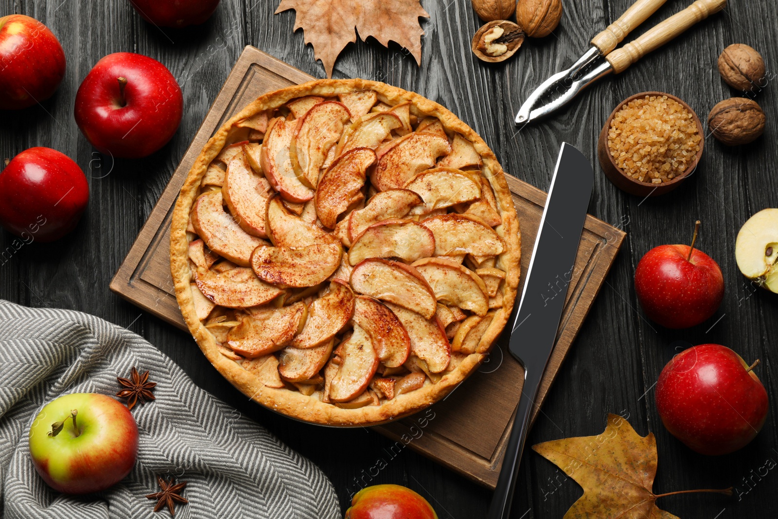 Photo of Delicious apple pie and ingredients on black wooden table, flat lay