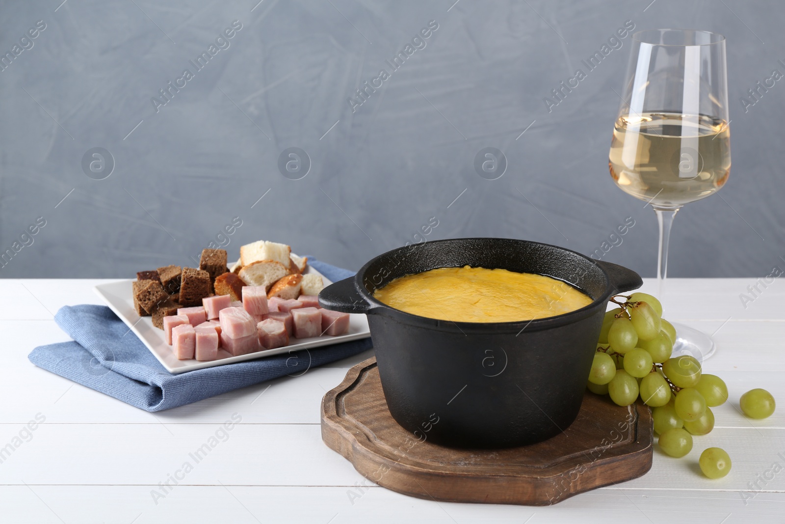 Photo of Fondue with tasty melted cheese, different products and aromatic wine in glass on white wooden table