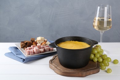 Fondue with tasty melted cheese, different products and aromatic wine in glass on white wooden table