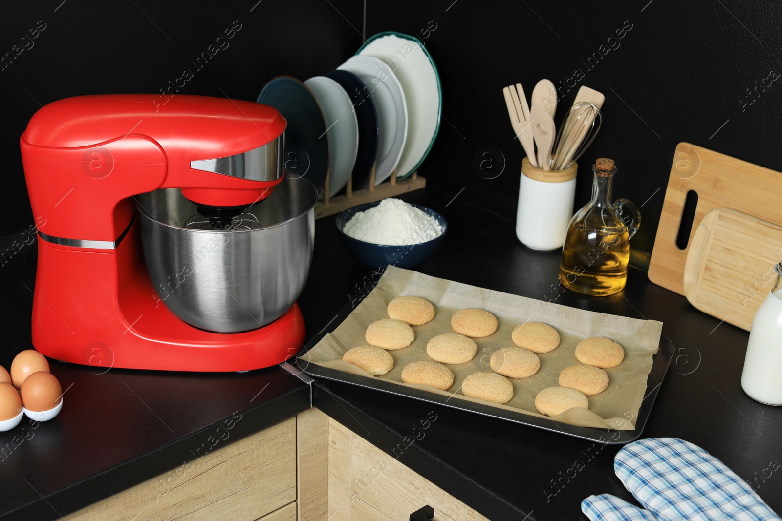 Photo of Modern stand mixer, ingredients, tableware and baked cookies on countertop in kitchen