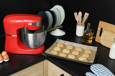 Photo of Modern stand mixer, ingredients, tableware and baked cookies on countertop in kitchen