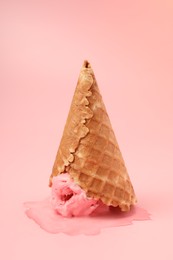 Melted ice cream in wafer cone on pink background