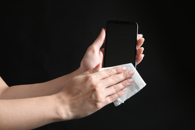 Photo of Woman cleaning smartphone with antiseptic wipe against black background, closeup