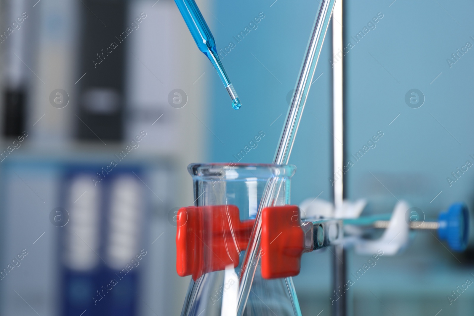 Photo of Laboratory analysis. Dripping blue liquid into flask on stand indoors, closeup