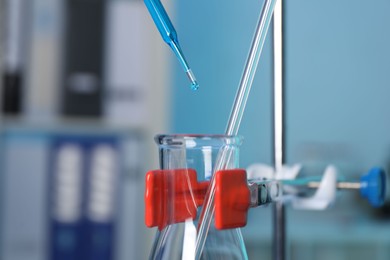 Laboratory analysis. Dripping blue liquid into flask on stand indoors, closeup