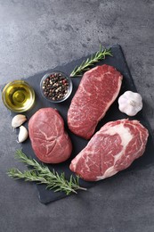 Photo of Raw beef steaks, oil and spices on grey background, top view