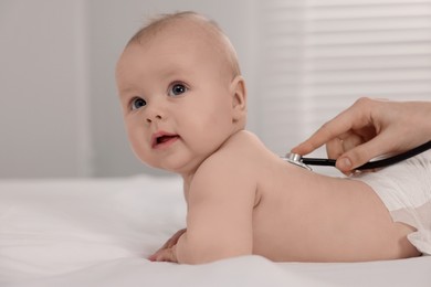 Photo of Pediatrician examining cute little baby with stethoscope in clinic, closeup