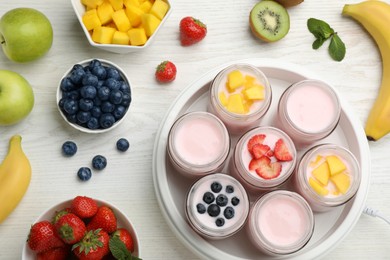 Yogurt maker with jars and different fruits on white wooden table, flat lay