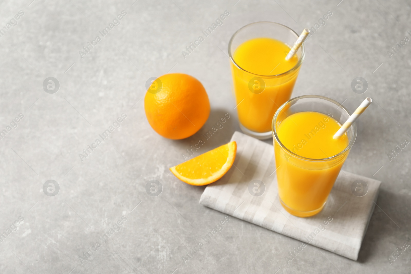 Photo of Glasses of orange juice and fresh fruits on light background