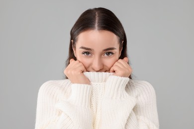 Beautiful young woman in stylish warm sweater on grey background