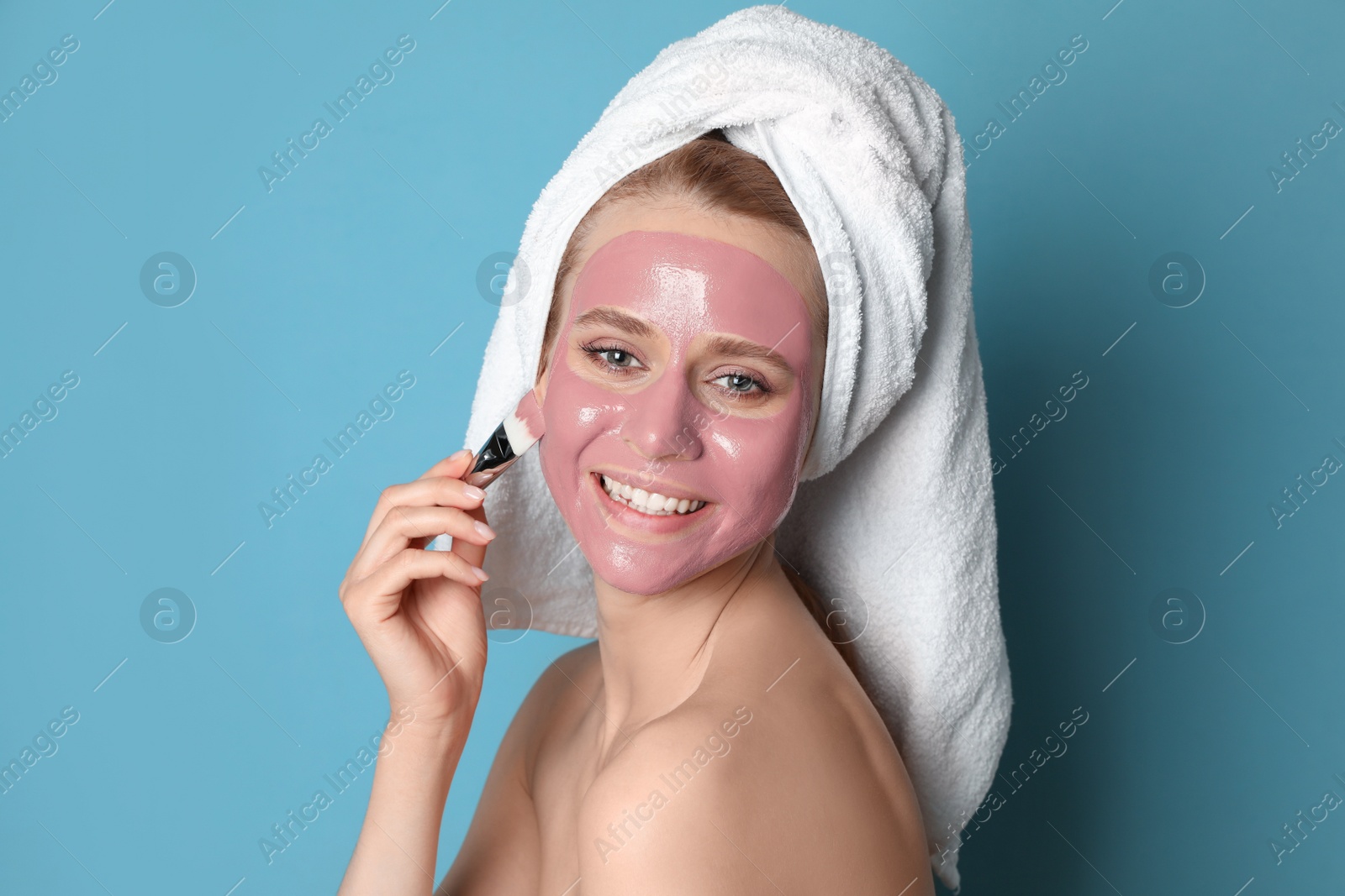 Photo of Young woman applying pomegranate face mask on light blue background