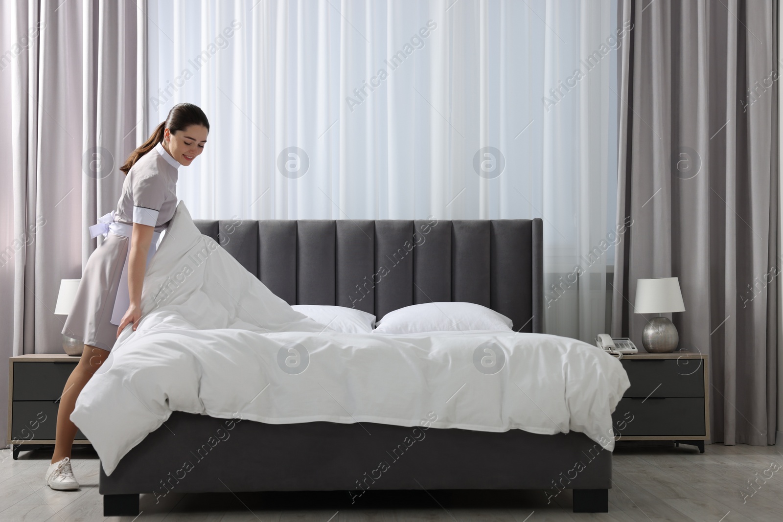 Photo of Young chambermaid making bed in hotel room. Space for text