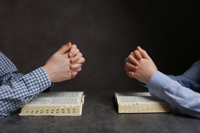 Photo of Couple praying over Bibles at grey table, closeup