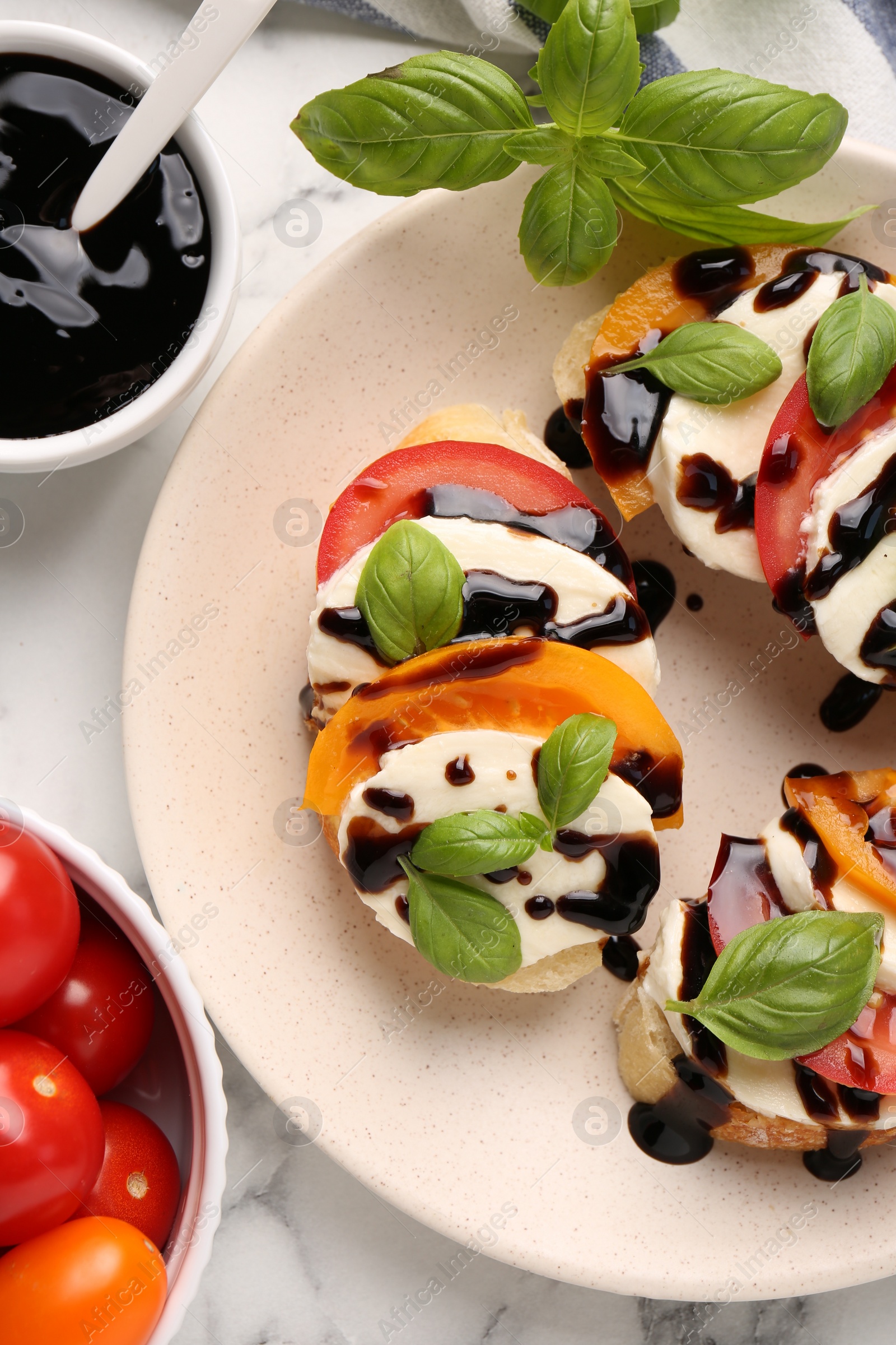 Photo of Delicious bruschettas with mozzarella cheese, tomatoes, balsamic vinegar and ingredients on white table, flat lay