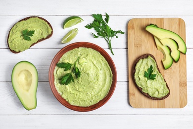 Flat lay composition with bowl of guacamole made of ripe avocados on white wooden table