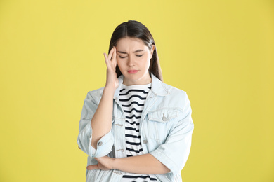 Young woman suffering from headache on yellow background