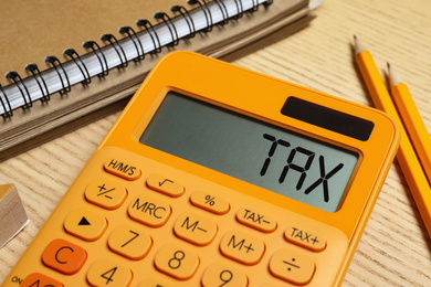 Image of Calculator with word Tax, notebook and pencils on wooden table, closeup