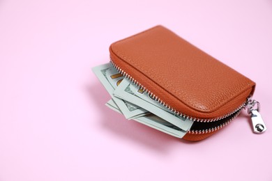 Photo of Stylish brown leather purse with dollar banknotes on pink background, closeup. Space for text