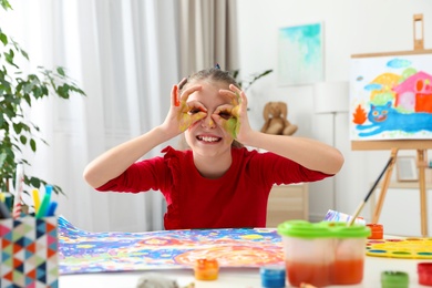 Little child making glasses with painted hands at table indoors