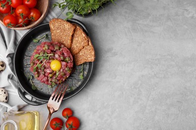 Photo of Tasty beef steak tartare served with yolk, capers and other accompaniments on light grey table, flat lay. Space for text