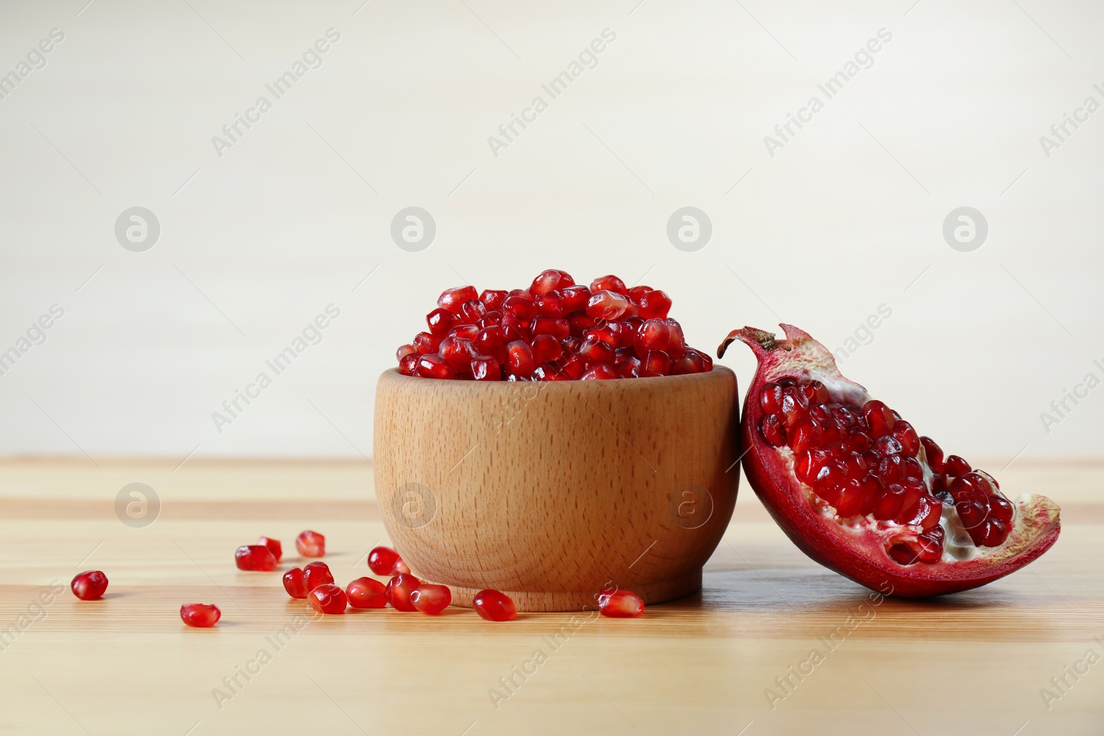 Photo of Bowl with pomegranate seeds and fresh fruit on table against light background