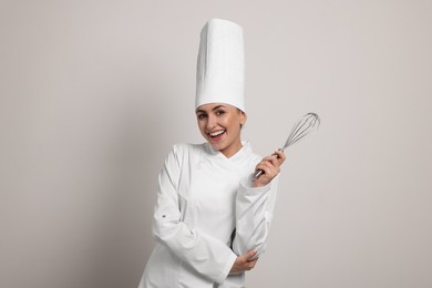 Photo of Happy professional confectioner in uniform holding whisk on light grey background