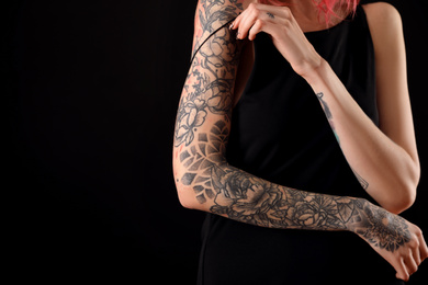 Photo of Beautiful woman with tattoos on arms against black background, closeup. Space for text