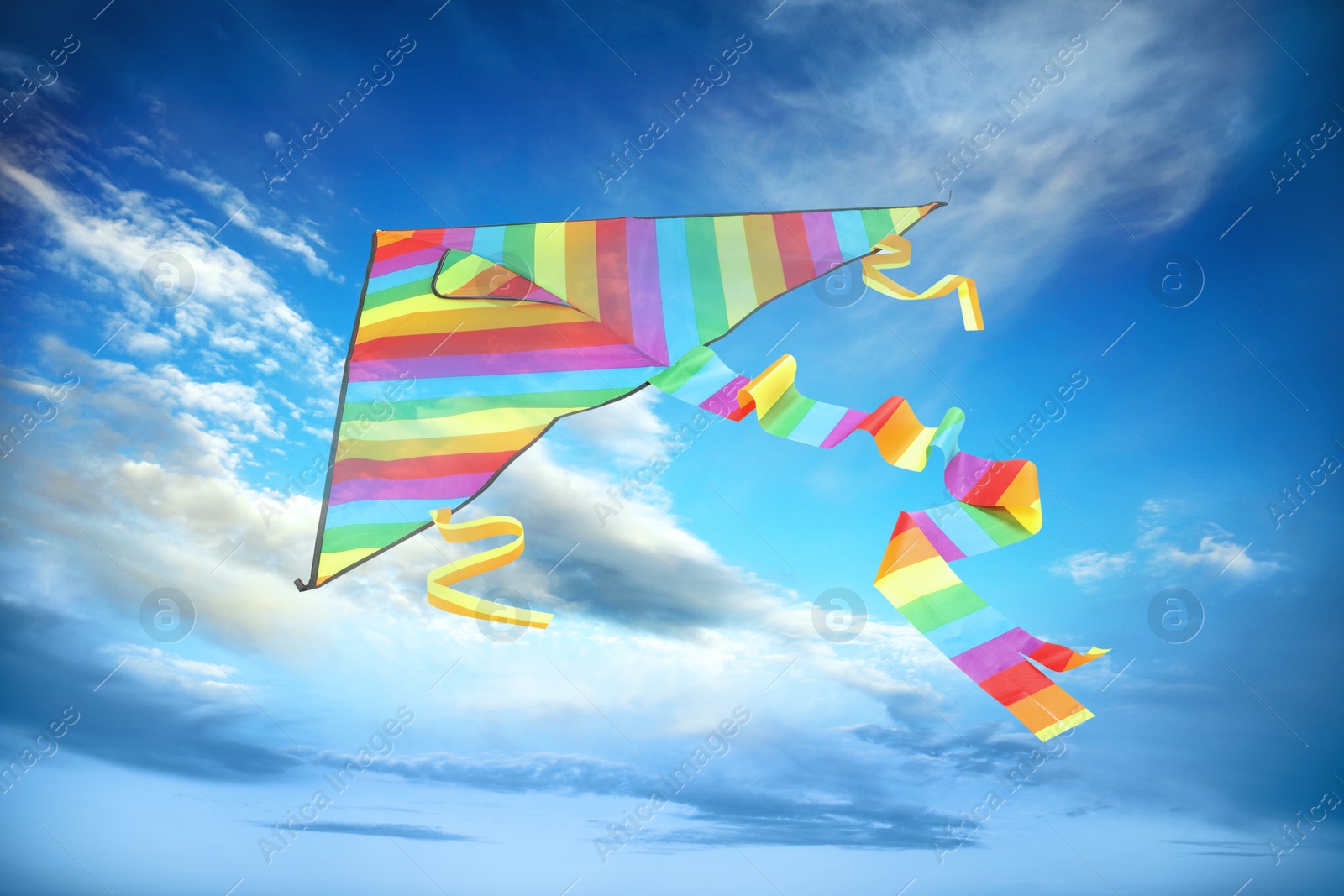 Image of Bright striped rainbow kite flying in blue sky on sunny day