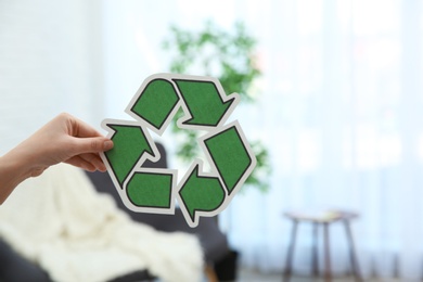 Woman holding recycling symbol on blurred background, closeup. Space for text