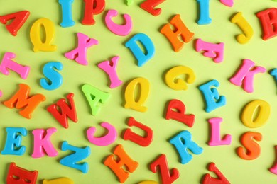 Many colorful magnetic letters on light green background, flat lay