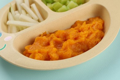 Photo of Healthy baby food. Section plate with delicious pumpkin puree and vegetables on light blue background, closeup