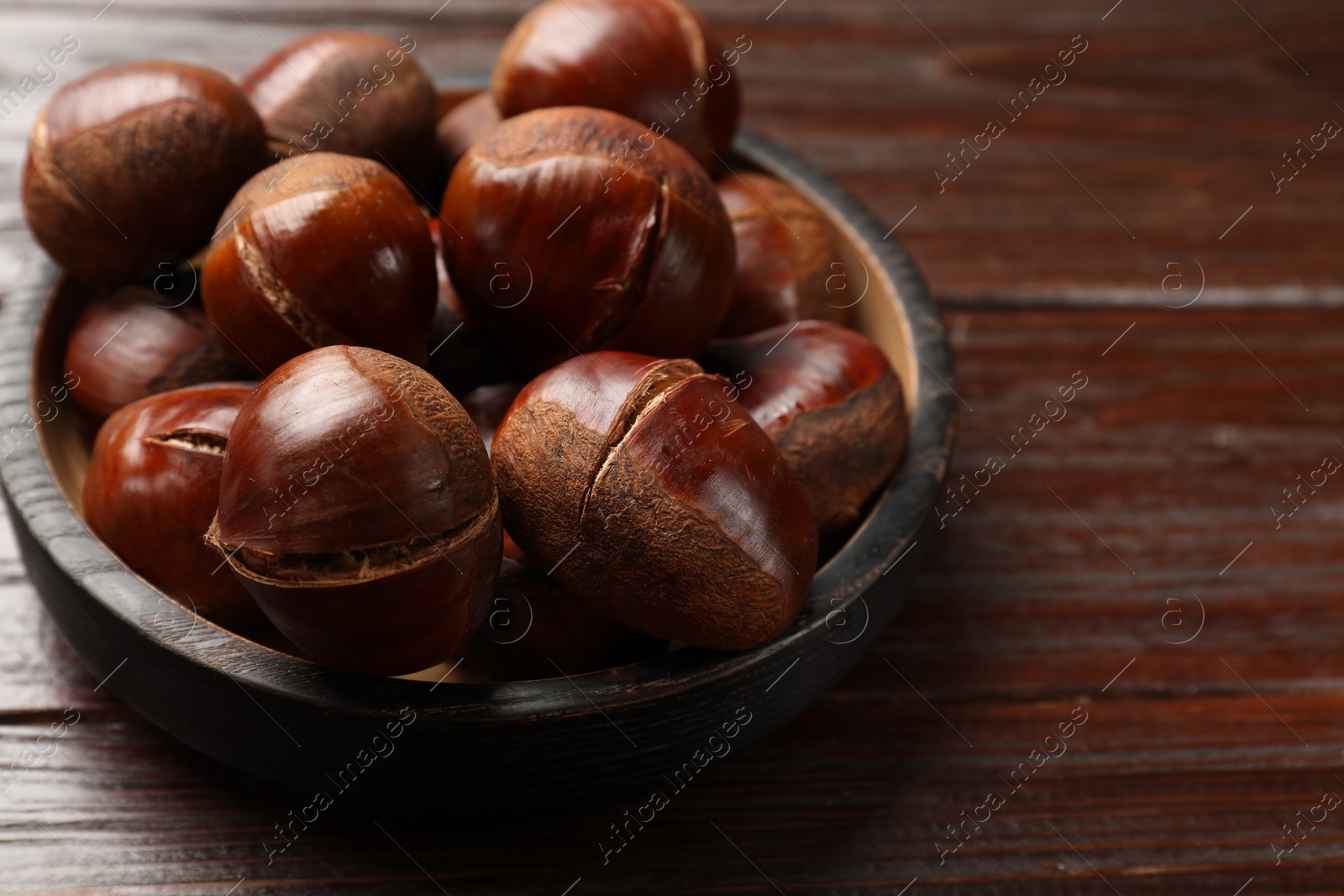 Photo of Roasted edible sweet chestnuts on wooden table, closeup. Space for text