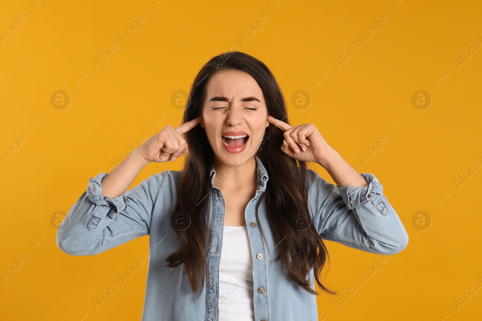 Photo of Emotional young woman covering ears with fingers on yellow background